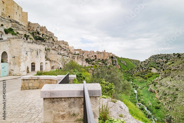 Fototapeta Matera, Italy. View of Via Madonna delle Virtù in the Sassi di Matera, Italy. In the distance, the Convento di Sant’Agostino crowns the hilltop. Below right flows the Gravina torrent.