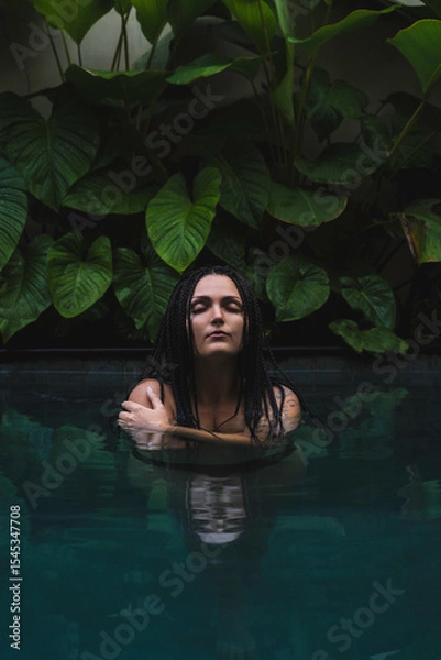Obraz A woman with braids enjoying in a pool, surrounded by lush tropical leaves in a serene and intimate moment in Ubud, Bali, Indonesia