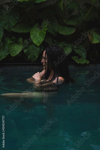 Obraz A woman with braids enjoying in a pool, surrounded by lush tropical leaves in a serene and intimate moment in Ubud, Bali, Indonesia