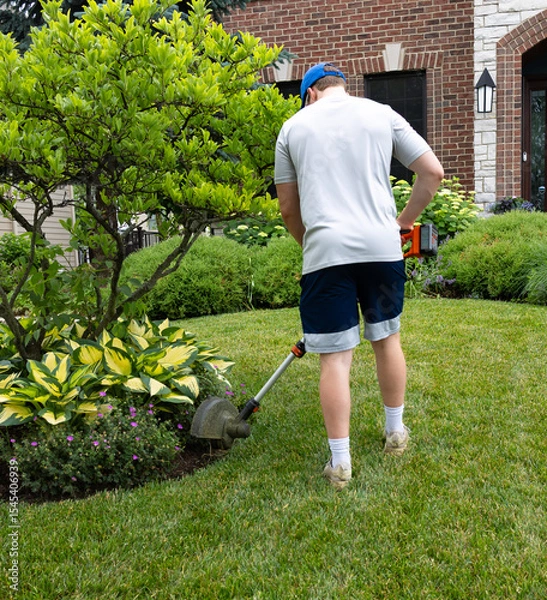 Obraz A self motivated teenage boy edges the garden  methodically carving clean lines between lawn and flowers. Sweat glistens as he works, shaping the soil with precision and pride in the hot, humid sun