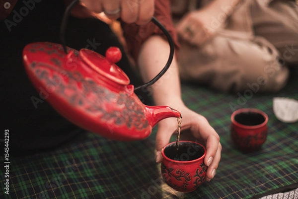 Obraz tea ceremony and tea drinking in nature. red teapot and red cups. green chinese tea is poured into a cup from a teapot. picnic with tea ceremony.