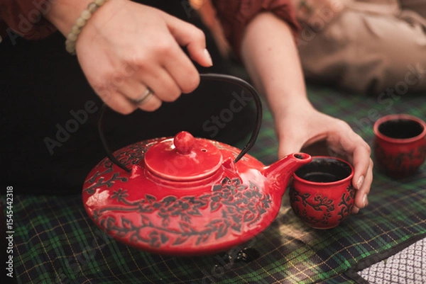 Obraz tea ceremony and tea drinking in nature. red teapot and red cups. green chinese tea is poured into a cup from a teapot. picnic with tea ceremony.