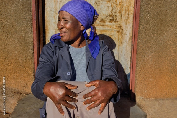 Fototapeta village single old african woman with headscarf sited in front of the house , in the yard, close portrait