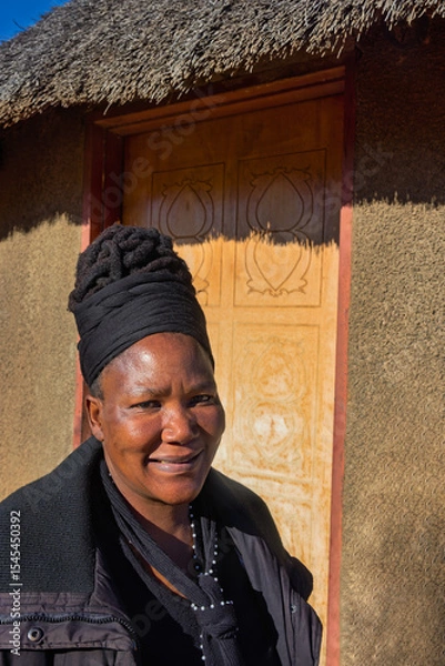Fototapeta village single old african woman with dreadlocks braids in a headscarf sited in front of the house , in the yard, close portrait