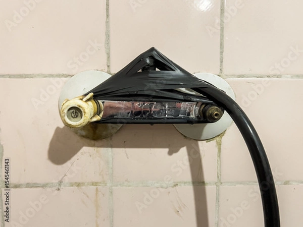 Obraz Provisionally repaired shower holder, wrapped with black insulating tape, on an old, pink, dirty tile wall, showing improvisation and negligence