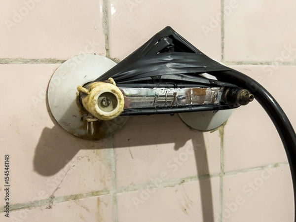 Obraz Provisionally repaired shower holder, wrapped with black insulating tape, on an old, pink, dirty tile wall, showing improvisation and negligence