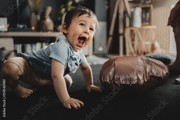 Obraz Cheerful child on the floor, smiling and full of energy, next to a copper balloon, in a warm, home environment