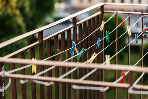 Obraz Empty clothes dryer with colorful paper clips on the balcony, with a blurred green background of urban surroundings