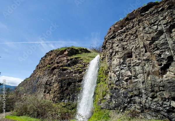 Fototapeta Rowland Lake Falls with wide swath of water crashing down between rough rocky walls such that the spray increases the local humidity enough to allow moss and other green foliage to grow on the cliff.