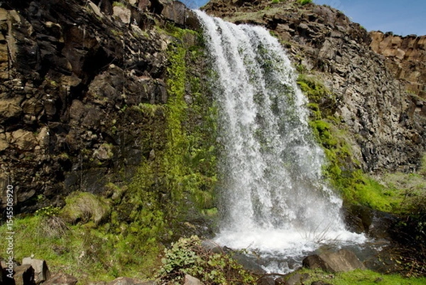 Fototapeta Rowland Lake Falls with wide swath of water crashing down between rough rocky walls such that the spray increases the local humidity enough to allow moss and other green foliage to grow on the cliff.