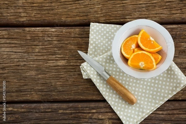 Fototapeta Orange slices in bowl with knife and napkin on table