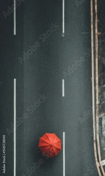 Obraz Overhead view of a solitary red umbrella on a dark asphalt road with lane markings