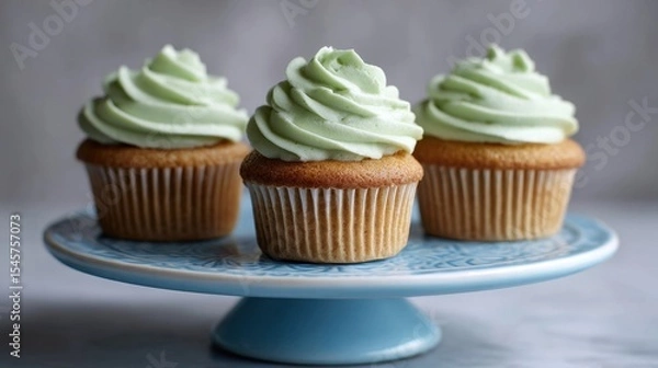 Fototapeta Three cupcakes with green frosting on a blue cake stand