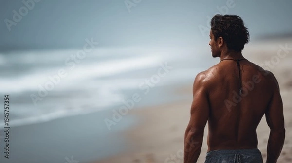 Fototapeta A man standing on a beach looking out at the ocean