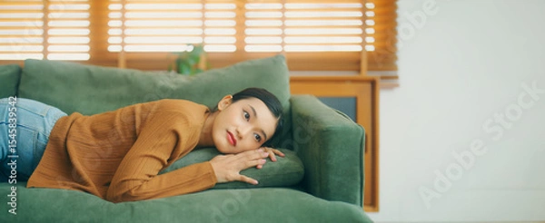 Fototapeta Asian woman resting at home on couch, feeling exhausted after work, lacking energy, or overworked, too tired, and lacking motivation