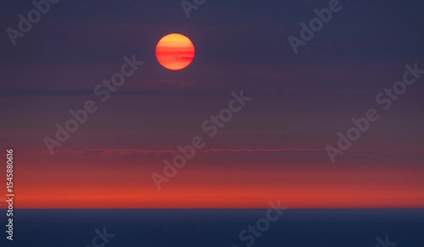 Fototapeta Sunset over the Norwegian Sea with the glowing sun touching the horizon above the silhouette of a distant ship. A dramatic seascape perfect as a bold and warm background image. View from cruise ship