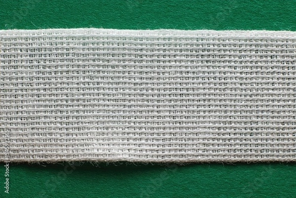 Fototapeta Close-up of a white woven fabric strip on a green background, showing its texture and slightly frayed edges