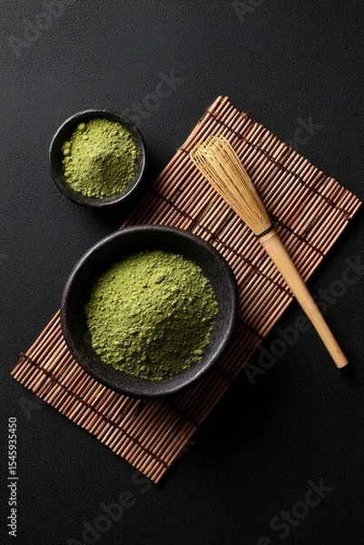 Fototapeta Overhead view of two bowls of vibrant green matcha powder, a bamboo whisk, and a bamboo mat on a dark surface