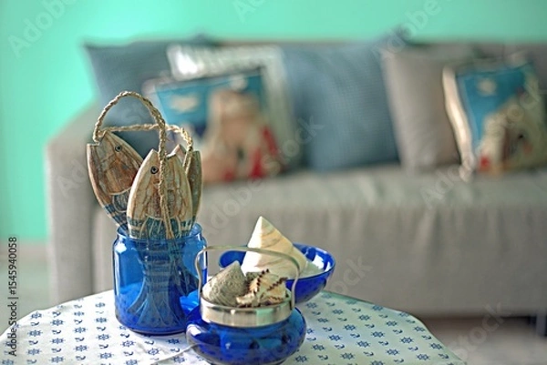 Fototapeta Marine style in the apartment interior - a sofa with pillows and a table with shells and fish figures.