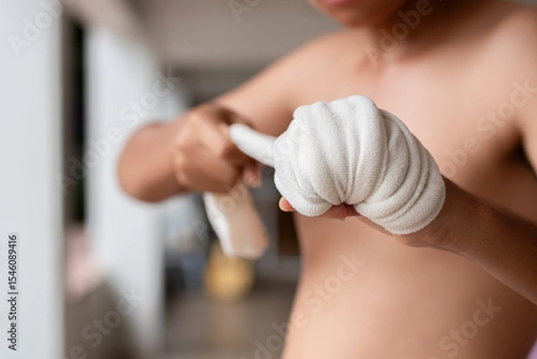 Fototapeta Close-up of a young Muay Thai fighter wrapping his hand with traditional cloth. The image captures detail and texture, highlighting strength, focus, and cultural authenticity.