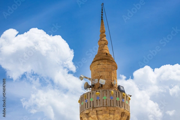 Fototapeta View of the top of a minaret with loudspeakers and CCTV cameras against a blue sky with white fluffy cumulus clouds
