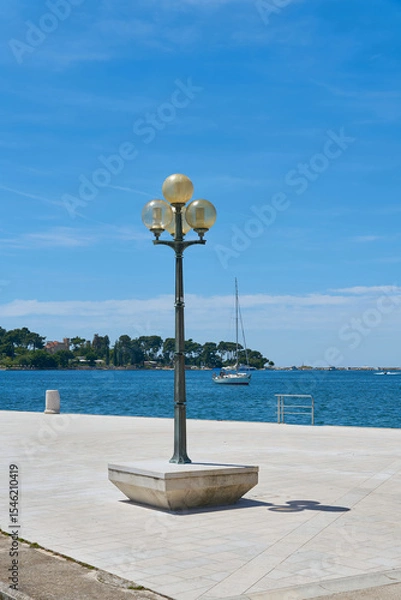 Obraz Laterne auf der Uferpromenade im Hafen von Porec in Kroatien. Im Hintergrund die Insel Sveti Nikola.