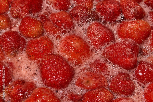 Fototapeta Homemade preparation of strawberry jam. Foam and juice when cooking strawberries. The process of making strawberry jam. Close-up of boiling strawberries.