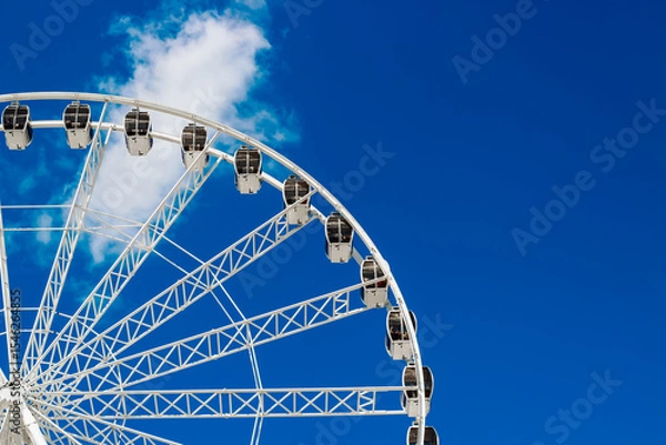 Obraz Bright Ferris wheel towers against a clear blue sky with white clouds during a sunny day