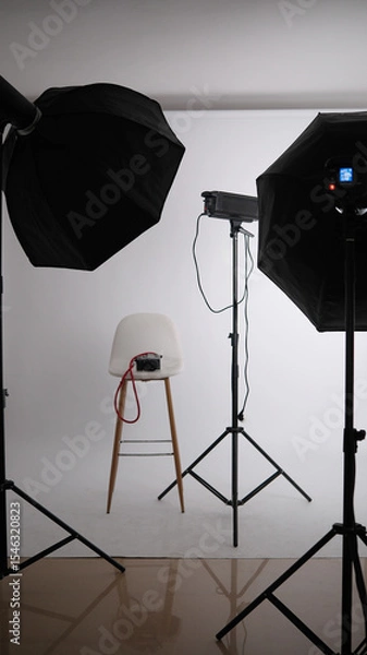 Fototapeta Empty stool surrounded by professional lighting equipment in photo studio. 