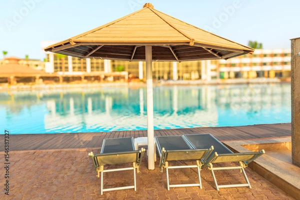 Obraz Sun loungers and umbrella by the pool with clear azure water in the tropics