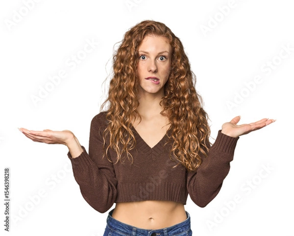 Fototapeta Simple redhead studio portrait confused and doubtful shrugging shoulders to hold a copy space.
