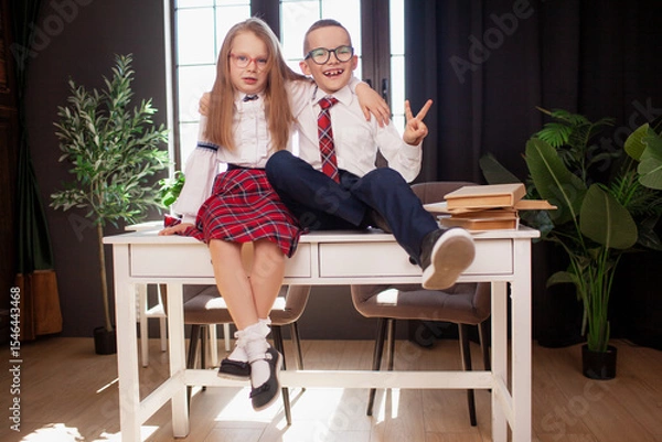 Fototapeta A 7-year-old child in glasses dressed in  school uniform poses at the school table indoor