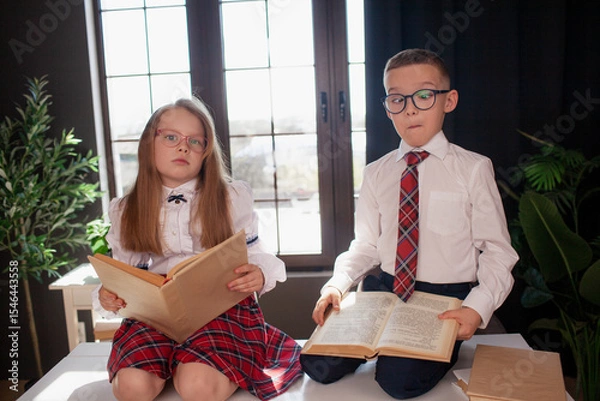 Fototapeta A 7-year-old child in glasses dressed in  school uniform poses at the school table indoor