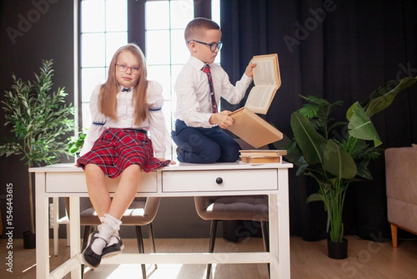 Fototapeta A 7-year-old child in glasses dressed in  school uniform poses at the school table indoor