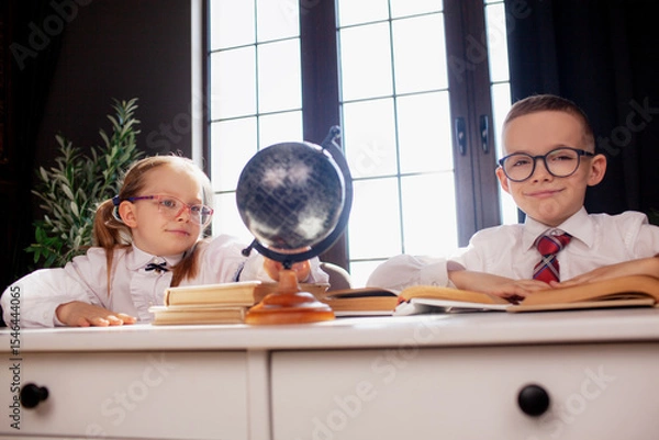 Fototapeta A 7-year-old child in glasses dressed in  school uniform poses at the school table indoor