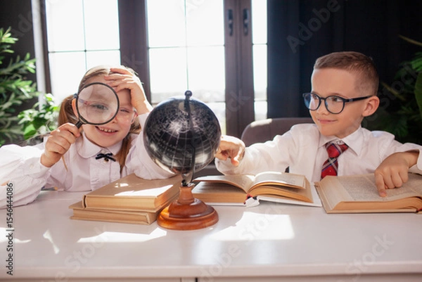Fototapeta A 7-year-old child in glasses and school uniform poses at the school table indoor