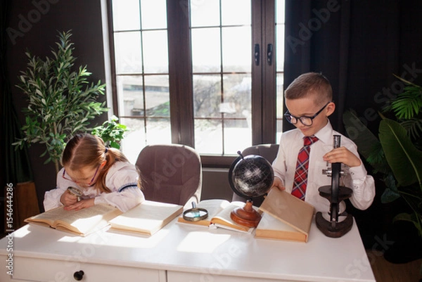 Fototapeta A 7-year-old child in glasses and school uniform poses at the school table indoor