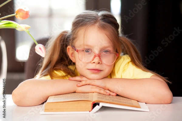 Fototapeta A 7-year-old child in glasses and  poses at the school table indoor