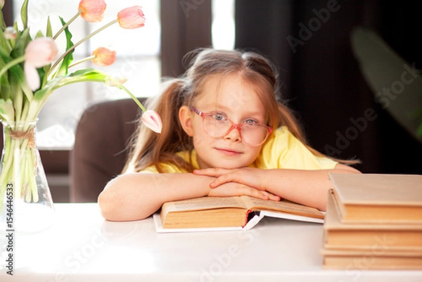 Fototapeta A 7-year-old child in glasses and  poses at the school table indoor
