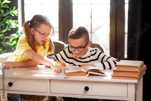 Fototapeta A 7-year-old child in glasses dressed in  school uniform poses at the school table indoor
