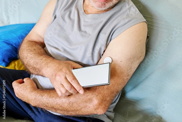 Fototapeta Unrecognizable mature man with diabetes and continuous glucose monitor on his arm using mobile app for checking his health