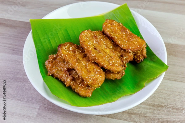 Fototapeta Crispy Thai fried bananas with sesame seeds served on a banana leaf in a white plate, Fried bananas is a traditional Asian snack with sweet, crunchy texture. Top view shot