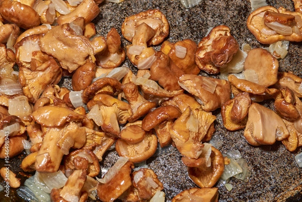 Fototapeta Hot mushroom dish – chanterelles fried with onions in oil. A fragrant dish of fried chanterelles and onions in a frying pan. A close–up of fried chanterelles is a simple and delicious meal.