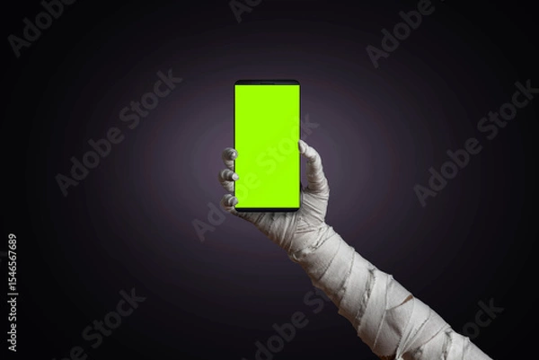Fototapeta Mummy's hand wrapped in bandages holding blank sign template smartphone with empty copy space screen. Horrible risen dead mummy monster for a Halloween horror concept