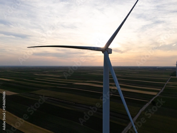 Fototapeta Aerial view of wind turbine on an agricultural filed at sunset. Close up of blades