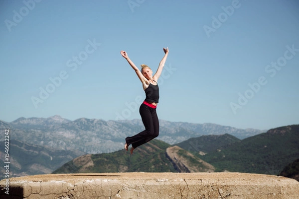 Fototapeta Joyful woman practicing yoga jump pose outdoors, surrounded by breathtaking mountain scenery, embodying freedom and vitality in nature