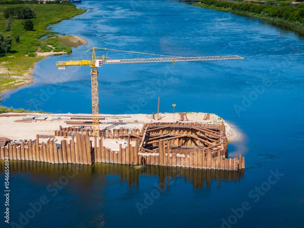 Obraz Construction site of new modern bridge construction in Kaunas, Lithuania. Aerial drone view of bridge connecting two shores of a river. Work progress