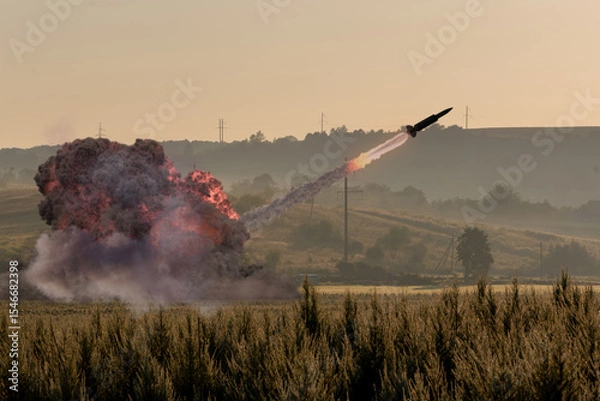 Obraz Launching a military rocket in the field - a trail of fire in the sky and puffs of smoke from the launch in the morning landscape.
