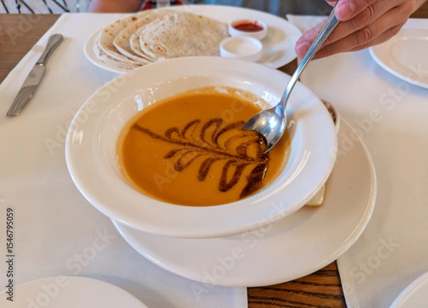 Obraz A person eating traditional Turkish red lentil soup, Mercimek Corbasi, garnished with spiced butter.First course of Turkish meal: A bowl of hot, creamy lentil soup being served at a restaurant table
