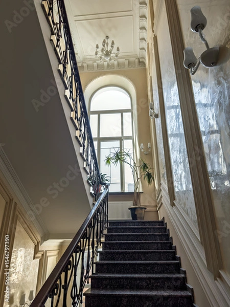 Obraz Elegant Interior of a Luxury Home with a Marble Staircase and a Large Arched Window. Grandeur of Classical Architecture: A Majestic Stairway with Marble Steps and Ornate Wrought Iron Railing